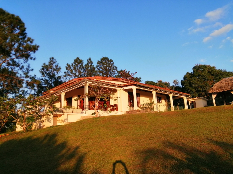 Private country casa with a tiled roof and columned porch on a green hillside in Cuba at golden hour