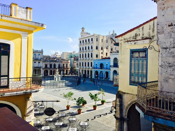 Balcony view over a sunlit Havana plaza framed by pastel colonial facades