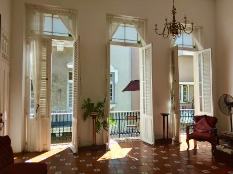 Sunlit colonial living room with tall shuttered doors opening onto balconies in a private Havana home