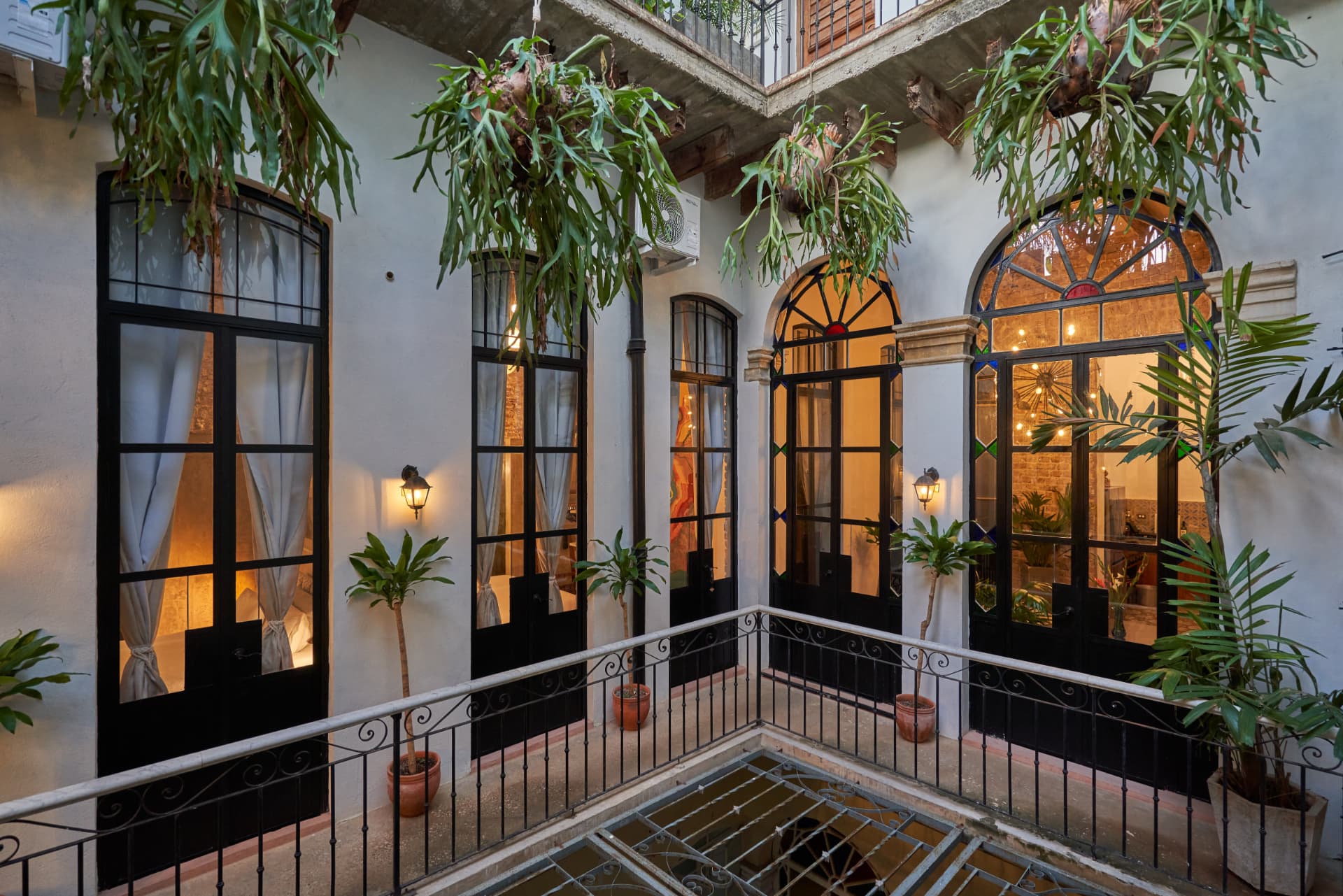 Interior courtyard balcony of a restored colonial casa in Cuba with arched stained-glass doors and hanging ferns